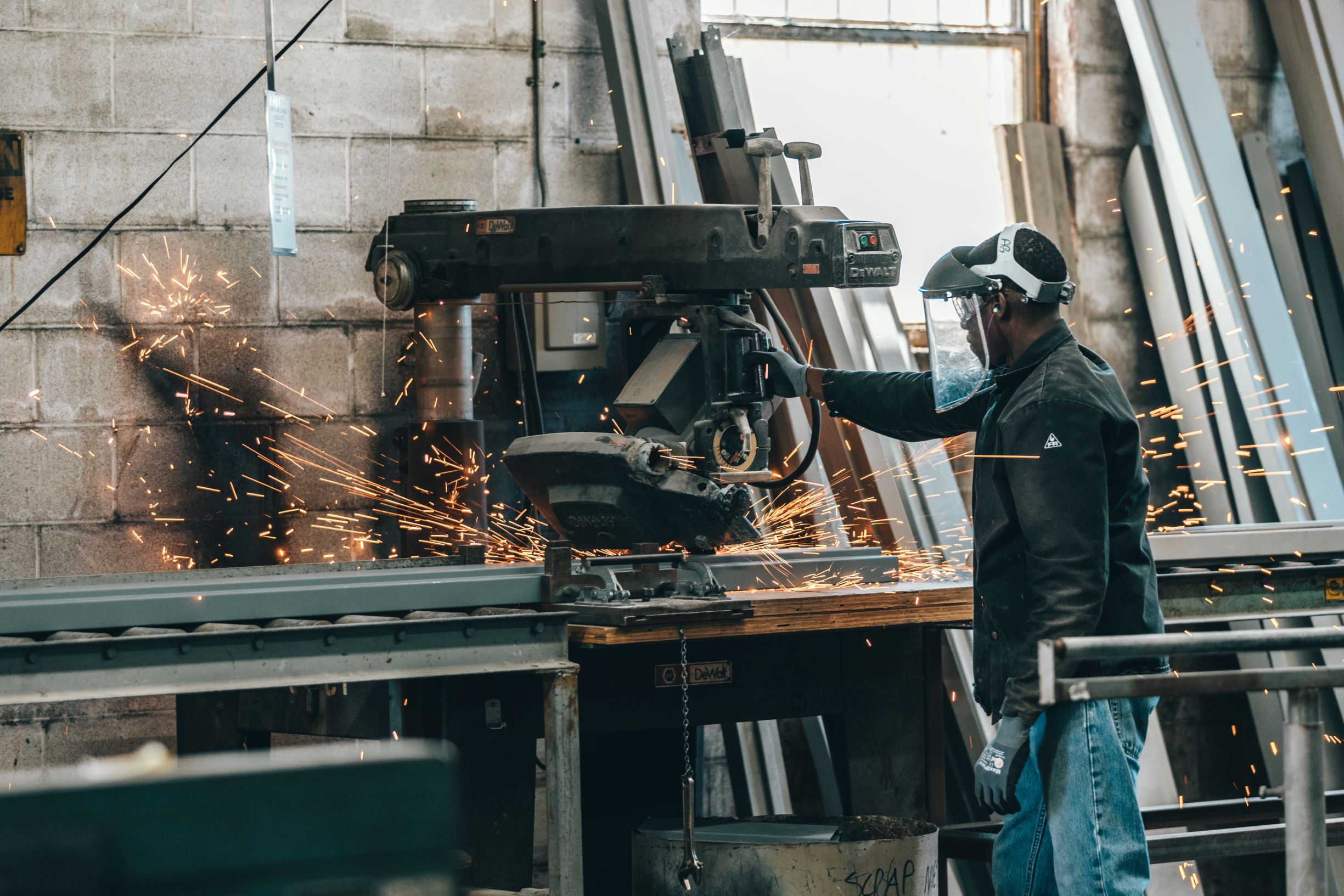 man in a manufacturing factory with industrial gloves and mask sawing mental with electric saw